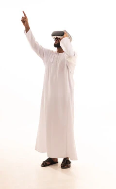 الاشارة بإصبع السبابة إلى شيء ما، استخدام الأجهزة التقنية الحديثة، التفاعل والاندماج مع الواقع الافتراضي، رؤية المشاهد الخيالية،بورتريه لشاب عربي خليجي عماني يرتدي الدشداشة والكمه يضع نظارات الفي آر، قضاء أوقات الفراغ بشكل ممتع، الجسم بالطول الكامل، خلفية بيضاء