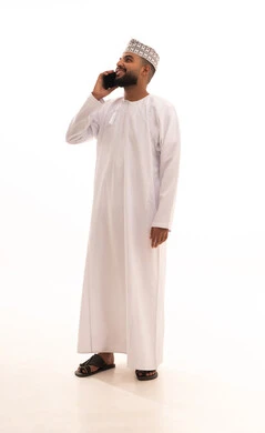 Gestures of joy upon hearing some news, making a phone call via mobile, a portrait of a young Arab Gulf Omani man wearing a dishdasha and kumma holding a mobile phone in his hand, a full-body image, white background.