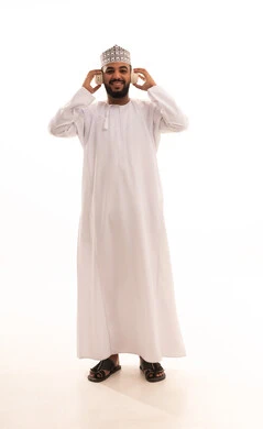 الاستماع إلى الموسيقى، إيماءات السعادة و الاندماج مع الأغنية، مواهب غنائية فنية، بورتريه لشاب عربي خليجي عماني مبتسم يرتدي الدشداشة و الكمة يضع الهيدفون, تسجيل مقطع صوتي غنائي، صورة الجسم بالكامل، خلفيه بيضاء