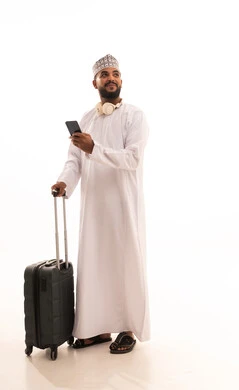 النظر الى شيء ما، تصفح تطبيقات الهاتف المحمول، الاستعداد لقضاء رحلة صيفية ممتعة، بورتريه لشاب عربي خليجي عماني يرتدي الدشداشه والكمه يمسك بيديه حقيبة السفر يقوم بمتابعة اخبار وسائل التواصل الاجتماعي ، الجسم بالطول الكامل، خلفية بيضاء