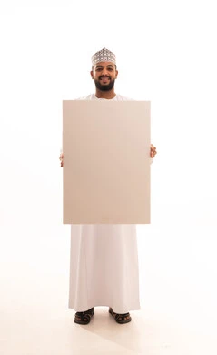 Using illustrative identification boards, a rectangular white mockup, a portrait of a young Arab Gulf Omani man wearing a dishdasha and kumma holding a blank rectangular white board in his hand, looking at the camera with gestures of joy and happiness, advertisements and marketing promotions, full-body image, white background.