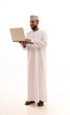 The concept of remote business management, preparing work-related reports, a portrait of a young Arab Gulf Omani man wearing a dishdasha and kumma holding a laptop in his hand, using modern technologies and devices to accomplish tasks, making video calls, full-body image, white background.