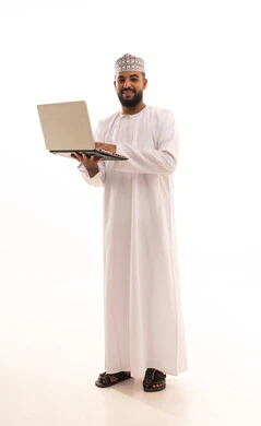 Preparing work-related reports, the concept of remote business management, a portrait of a young Arab Gulf Omani man wearing a dishdasha and kumma holding a laptop in his hand, using modern technologies and devices to accomplish tasks, making video calls, full-body image, white background.
