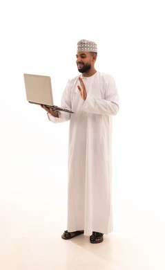 رفع كف الايد بتعابير السلام و التحية، اعداد التقارير الخاصة بالعمل، مفهوم إدارة الأعمال عن بعد، بورتريه لشاب عربي خليجي عماني يرتدي الدشداشة و الكمه يحمل بيده جهاز اللابتوب المحمول، إجراء مكالمات فيديو, صورة الجسم بالطول الكامل، خلفية بيضاء