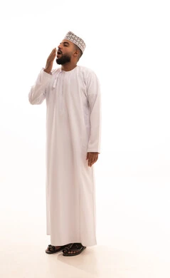 الإحساس بالإرهاق والتعب، بورتريه لشاب عربي خليجي عماني يرتدي الدشداشة والكمه يضع يديه على فمه بإيماءات النعاس والحاجة الى النوم والراحة، تعابير التثاؤب والخمول والرغبة في النوم، صورة الجسم بالطول الكامل، خلفية بيضاء