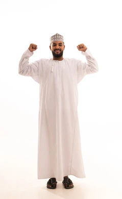 التمتع بالبنية الجسدية القوية، اللياقة البدنية والجسم الصحي المتين، بورتريه مقرب لرجل عربي خليجي عماني يرتدي الدشداشة والكمه يقوم بعرض عضلات يديه ينظر الى الكاميرا بإيماءات القوة، صورة الجسم بالطول الكامل، خلفية بيضاء