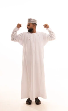 اللياقة البدنية والجسم الصحي المتين، بورتريه مقرب لرجل عربي خليجي عماني يرتدي الدشداشة والكمه يقوم بعرض عضلات يديه ينظر الى الكاميرا بإيماءات القوة، التمتع بالبنية الجسدية القوية، صورة الجسم بالطول الكامل، خلفية بيضاء