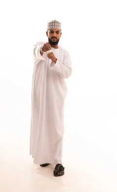 Increasing muscle endurance, mastering the art of boxing, a portrait of a young Arab Gulf Omani man wearing a dishdasha and kumma raising his fists in gestures of strength, practicing martial arts, full-body image, white background.