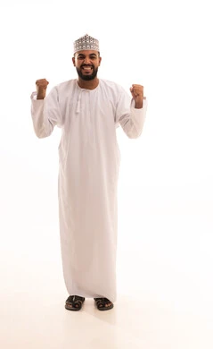 Victory, winning, and success, the concept of achievement and reaching goals, a portrait of a smiling young Arab Gulf Omani man wearing a dishdasha and kumma, raising his fists up, looking at the camera with gestures of joy and happiness, feeling of happiness and strength, full-body image, white background.