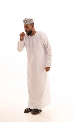 Feeling sick and coughing, influenza and pneumonia, a portrait of an Omani Arab man wearing a dishdasha and kumma suffering from a cough, infected with the coronavirus, feeling tired and exhausted, full-body shot, white background.