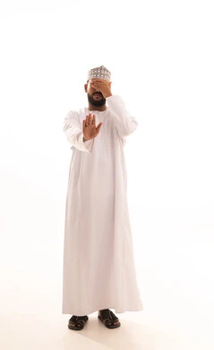 Gestures of fear, anxiety, and discomfort about something, rejection and refusal of harm, a portrait of an Omani Arab man wearing a dishdasha and kumma covering his eye and raising his other hand up in a stop gesture, a request to stop and refrain from doing something, full-body, white background.