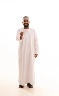 Display of an identification card, a blank rectangular white mock-up, a portrait of a young Arab Gulf Omani man wearing a dishdasha and a kumma holding an ID card in his hand, standing upright and looking at the camera with gestures of joy and happiness, full body, white background.