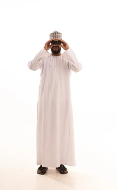 النظر إلى المسافات البعيدة باستخدام التلسكوب، إيماءات الفرح والسرور، حب المغامرة والاستكشاف، بورتريه لشاب عربي خليجي عماني يرتدي الدشداشة والكمه ينظر من خلال المنظور ثنائي العينين (التلسكوب) ، صورة الجسم بالطول الكامل، خلفية بيضاء