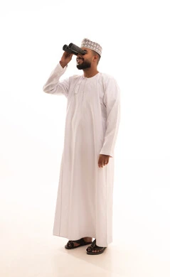 إيماءات الفرح والسرور، رؤية الاشياء البعيدة عبر المنظار، حب المغامرة والاستكشاف، بورتريه لشاب عربي خليجي عماني يرتدي الدشداشة والكمه ينظر من خلال المنظور ثنائي العينين (التلسكوب) ، صورة الجسم بالطول الكامل، خلفية بيضاء