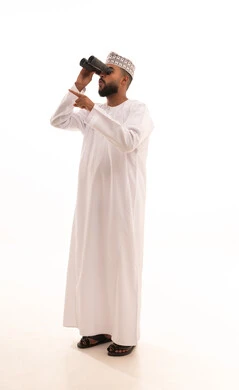 Love for adventure and exploration, seeing distant things through a telescope, a portrait of a young Arab Gulf Omani man wearing a dishdasha and kumma looking through a binocular (telescope) pointing with his index finger at something with gestures of joy and happiness, full-body image, white background.