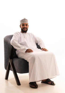 مفهوم الاسترخاء والاستمتاع بالأجواء الهادئة، بورتريه لرجل عربي خليجي عماني يرتدي الدشداشه والكمه يجلس على كرسي مريح، تعابير وإيماءات الراحة، خلفية بيضاء