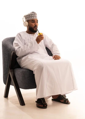إيماءات المفاجأة والاندماج، الاستمتاع بمشاهدة الأفلام، الحصول على عصير صيفي بارد ومنعش، بورتريه لرجل عربي عماني خليجي يرتدي الدشداشة و الكمة و سماعات الهيدفون ويمسك بيده كأس من المشروب المفضل، خلفية بيضاء