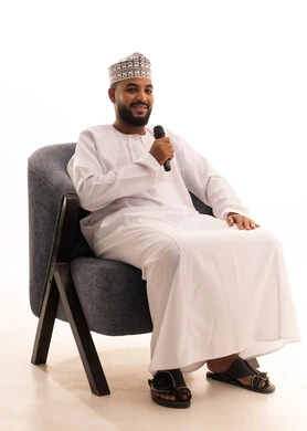 تقديم العروضات المسرحية، الاستمتاع بأداء المواهب الصوتية، بورتريه لرجل عربي عماني خليجي يرتدي الدشداشة و الكمة يمسك بيده المايكروفون، تسجيل مقطع صوتي غنائي، خلفيه بيضاء