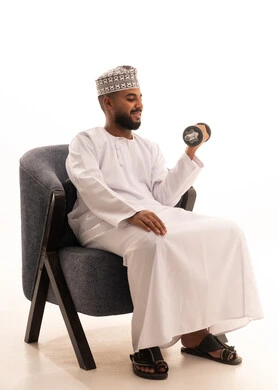 بناء عضلات الجسم وتقويتها، نشاط بدني للمحافظة على اللياقة الجسدية، رفع الأوزان الحديدية الثقيلة، بورتريه لرجل عربي عماني خليجي يرتدي الدشداشة و الكمة يجلس على كرسي يحمل بيده الأثقال ، الاهتمام باللياقة والصحة الجسدية، خلفية بيضاء