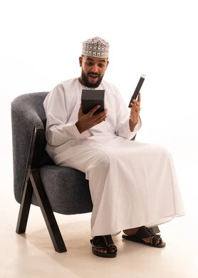 Gestures of happiness and surprise at receiving a gift, the concept of surprise and gifting, the art of carefully selecting gifts, a portrait of an Arab Gulf Omani man wearing a kumma and dishdasha sitting on a chair and opening a box with expressions of joy and delight, white background. Gestures of happiness and surprise at receiving a gift, the concept of surprise and gifting, the art of carefully selecting gifts, a portrait of an Arab Gulf Omani man wearing a kumma and dishdasha sitting on a chair and opening a box with expressions of joy and delight, white background.