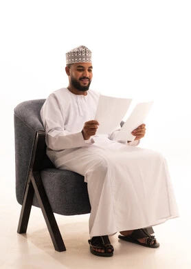 Reviewing the meeting results, feasibility study of the work, taking notes and preparing daily reports, a portrait of an Arab Gulf Omani man wearing a dishdasha and kumma sitting on a chair holding a set of white papers with gestures of thinking and focus, full body, white background.