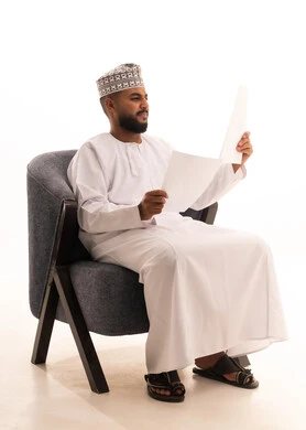 Feasibility study of the work, taking notes and preparing daily reports, reviewing meeting results, a portrait of an Arab Gulf Omani man wearing a dishdasha and kumma sitting on a chair holding a set of white papers with gestures of thinking and focus, full body, white background.