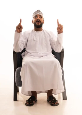The indication and clarification of something, a portrait of an Omani Arab man wearing a dishdasha and kumma, pointing with his index fingers upwards with expressions of this place here, specifying a certain location, white background.