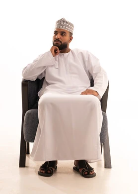 إيجاد الحل لمشكلة ما، التمعن والتركيز و التخطيط للمستقبل، بورتريه لرجل عربي خليجي عماني يرتدي الدشداشة و الكمة يجلس على كرسي يضع يده تحت ذقنه بإيماءات التامل والتفكير، مفهوم شرود الذهن، خلفية بيضاء