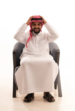 The feeling of astonishment and amazement, remembering something, a portrait of a Saudi Arabian Gulf man wearing traditional attire and a ghutrah sitting on a chair with his hands on his head in gestures of surprise and wonder, looking at the camera with gestures of shock, surprised by a specific situation, white background.