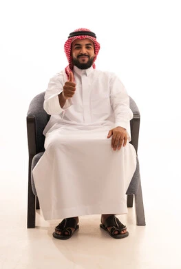 Approval, satisfaction, and acceptance, expressing quality and craftsmanship, a portrait of a Saudi Arabian Gulf man wearing traditional attire and a ghutrah, sitting on a chair, raising his hands with gestures of quality, excellence, and distinction, with a white background.