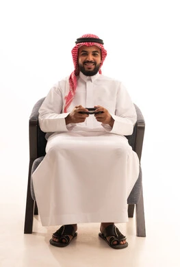 Gestures of interaction and integration, enjoying modern technologies and technology, a portrait of an Arab Gulf Saudi man wearing traditional attire and a ghutrah holding a game controller with a look of joy, the concept of fun and entertainment, spending enjoyable time playing video games, white background.