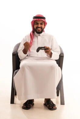 قضاء وقت ممتع في اللعب بألعاب الفيديو، إيماءات الفوز والانتصار, بورتريه لرجل عربي خليجي سعودي يرتدي الثوب التقليدي والشماغ يمسك عصا التحكم يرفع قبضة يده بتعابير الحماس، مفهوم المتعة والتسلية، الاستمتاع بالتقنيات والتكنولوجيا الحديثة، خلفية بيضاء