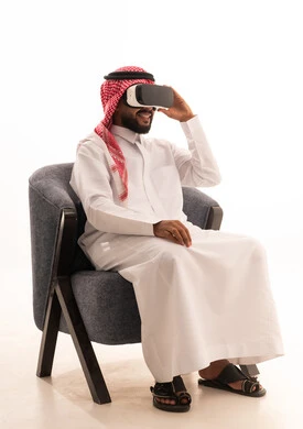 التفاعل والاندماج مع الواقع الافتراضي، استخدام الأجهزة التقنية الحديثة، رؤية المشاهد الخيالية، بورتريه لرجل عربي خليجي سعودي يرتدي الثوب التقليدي يجلس على كرسي يضع نظارات الفي آر، قضاء أوقات الفراغ بشكل ممتع، خلفية بيضاء
