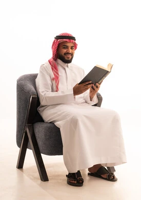 قضاء أوقات الفراغ بالأنشطة المفيدة، الاستمتاع بممارسة هواية المطالعة, بورتريه لرجل عربي خليجي سعودي يرتدي الثوب التقليدي والشماغ يجلس على كرسي  يقوم بقراءة الكتاب, مفهوم التعلم والتفوق والاجتهاد، خلفية بيضاء