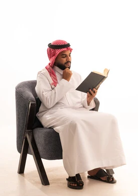 الاستمتاع بممارسة هواية المطالعة، التفكير فى شيء ما , بورتريه لرجل عربي خليجي سعودي يرتدي الثوب التقليدي والشماغ يجلس على كرسي  يقوم بقراءة الكتاب, قضاء أوقات الفراغ بالأنشطة المفيدة, مفهوم التعلم والتفوق والاجتهاد، خلفية بيضاء