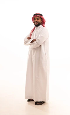 Standing with crossed arms, the concept of masculinity, strength, and self-confidence, a portrait of a Saudi Arabian Gulf man wearing a ghutrah and traditional attire looking at the camera with gestures of joy and happiness, attention to elegance and appearance, full-body, white background.