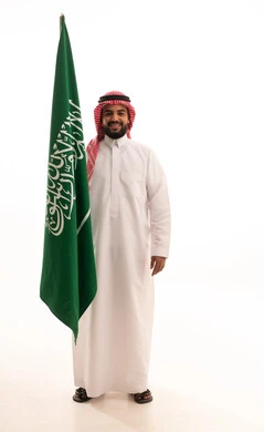 ايماءات السعادة و السرور، الفخر و الاعتزاز بالانتماء للمملكة, بورتريه لرجل عربي سعودي خليجي يرتدي الشماغ والثوب التقليدي يحمل بيده علم السعودية , يوم العلم 11مارس، الاحتفال بذكرى اليوم الوطني السعودي 8 ربيع الأول, الجسم بالطول الكامل، خلفية بيضاء
