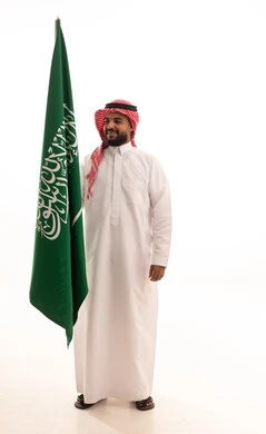 الفخر و الاعتزاز بالانتماء للمملكة, بورتريه لرجل عربي سعودي خليجي مبتسم يرتدي الشماغ والثوب التقليدي يحمل بيده علم السعودية , يوم العلم 11مارس، الاحتفال بذكرى اليوم الوطني السعودي 8 ربيع الأول, الجسم بالطول الكامل، خلفية بيضاء