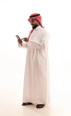 The evolution of technology and modern techniques, browsing social media sites on the internet, a portrait of an Arab Saudi Gulf man wearing a ghutrah and traditional thobe using a mobile phone, making video calls via the mobile, full-body image, white background.