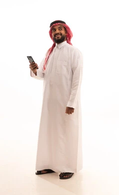 Looking at something with expressions of happiness and joy, the development of technology and modern techniques, browsing social media sites on the internet, a portrait of an Arab Saudi Gulf man wearing a ghutrah and traditional thobe using a mobile phone, full-body image, white background.