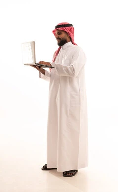 اجراء مكالمة فيديو عبر الانترنت، إنجاز مهام العمل عن بعد, استخدام الأجهزة التقنية الحديثة والمتطورة, بورتريه لرجل عربي خليجي سعودي يرتدي الشماغ والثوب التقليدي يقوم باستعمال جهاز الحاسوب المحمول,  الجسم بالطول الكامل، خلفية بيضاء