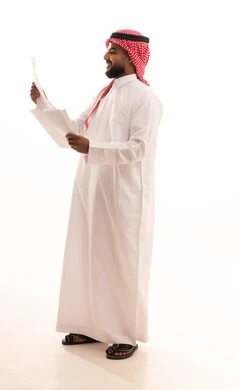 تعابير الفتكير والتركيز، التدقيق في قراءة الملاحظات، اعداد التقارير الخاصة بالعمل، بورتريه لرجل عربي خليجي سعودي يرتدي الشماغ والثوب التقليدي يحمل بيده مجموعة من الوثائق والاوراق البيضاء، مراجعة ومتابعة الخطط والمشاريع بايماءات السعادة، صورة الجسم بالكامل، خلفية بيضاء