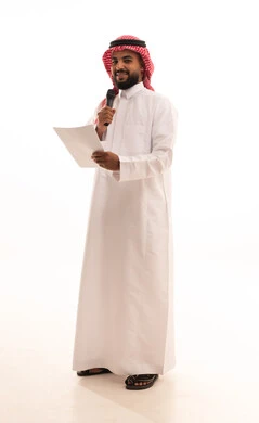 Giving lectures and holding seminars, exchanging dialogue and benefiting from experiences, a portrait of a Saudi Arabian Gulf Arab man wearing a ghutrah and traditional thobe holding a microphone and a set of papers, working in presenting segments and entertainment programs, full-body, white background.