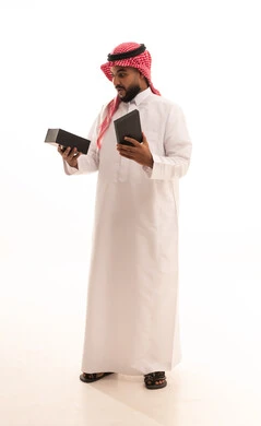 The concept of gratitude and appreciation, giving gifts during holidays and special occasions, expressing love, appreciation, and respect, a portrait of a Saudi Arabian Gulf man wearing a ghutrah and traditional thobe holding a gift box looking at it with gestures of surprise and shock, full-body, white background. The concept of gratitude and appreciation, giving gifts during holidays and special occasions, expressing love, appreciation, and respect, a portrait of a Saudi Arabian Gulf man wearing a ghutrah and traditional thobe holding a gift box looking at it with gestures of surprise and shock, full-body, white background.