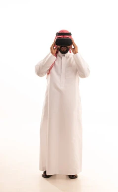 استخدام الأجهزة التقنية الحديثة، الاندماج ومحاكاة العالم الخيالي، المتعة والتسلية بالمشاهدة عبر نظارة الواقع الافتراضي، بورتريه لرجل عربي خليجي سعودي يرتدي الشماغ والثوب التقليدي يضع نظارات ثلاثية الأبعاد (الفي ار) ، الجسم بالطول الكامل، خلفية بيضاء