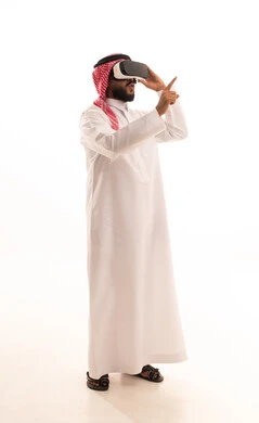 الاشارة الى شيء ما، المتعة والتسلية بالمشاهدة عبر نظارة الواقع الافتراضي، الاندماج ومحاكاة العالم الخيالي، بورتريه لرجل عربي خليجي سعودي يرتدي الشماغ والثوب التقليدي يضع نظارات ثلاثية الأبعاد (الفي ار), التطور التقني والتكنولوجي ، الجسم بالطول الكامل، خلفية بيضاء