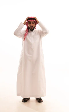 الانزعاج عند سماع خبر سيء ,النظر الى الكاميرا بتعابير التعجب, الوقوع في مصيبة, الصدمة و المفاجأة برؤية شيء ما، بورتريه لرجل عربي خليجي سعودي يرتدي الشماغ والثوب التقليدي يضع يديه على رأسه بتعابير الدهشة و الذهول، صورة الجسم بالطول الكامل، خلفية بيضاء