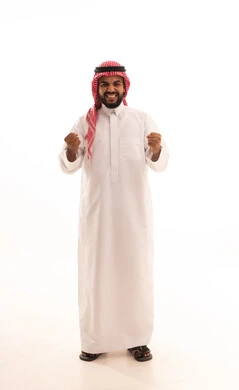 الانتصار والفوز والنجاح،مفهوم الانجاز وتحقيق الاهداف، بورتريه لرجل عربي خليجي سعودي مبتسم يرتدي الشماغ والثوب التقليدي ينظر الى الكاميرا يرفع قبضة يديه للاعلى بإيماءات الفرح والسرور, الشعور بالسعادة والقوة، الجسم بالطول الكامل، خلفية بيضاء