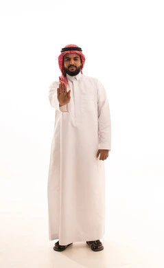 The concept of rejection, refusal, and discomfort, gestures of firmness and seriousness, a request to stop and not approach, a portrait of a Saudi Arabian Gulf man wearing a ghutrah and traditional thobe, pointing his hand upwards with expressions of forbidding an action, full-body, white background.