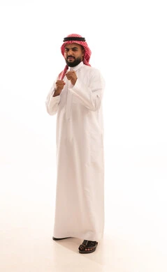ممارسة رياضة الدفاع عن النفس، إتقان فنون الملاكمة، تعزيز صحة العظام والمفاصل، زيادة قدرة العضلات على التحمل، بورتريه لرجل عربي خليجي سعودي يرتدي الثوب التقليدي والشماغ يرفع قبضات يديه بإيماءات القوة، الطول الكامل للجسم، خلفية بيضاء